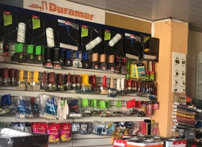 Parede da DF Tintas com rolos de pintura, pincéis, trinchas e luvas no painel Duramar